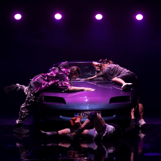 Artists laying on top of and in front of a car.