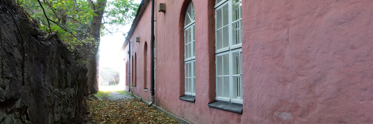 Rosa byggnad med välvda fönster och ett stort träd