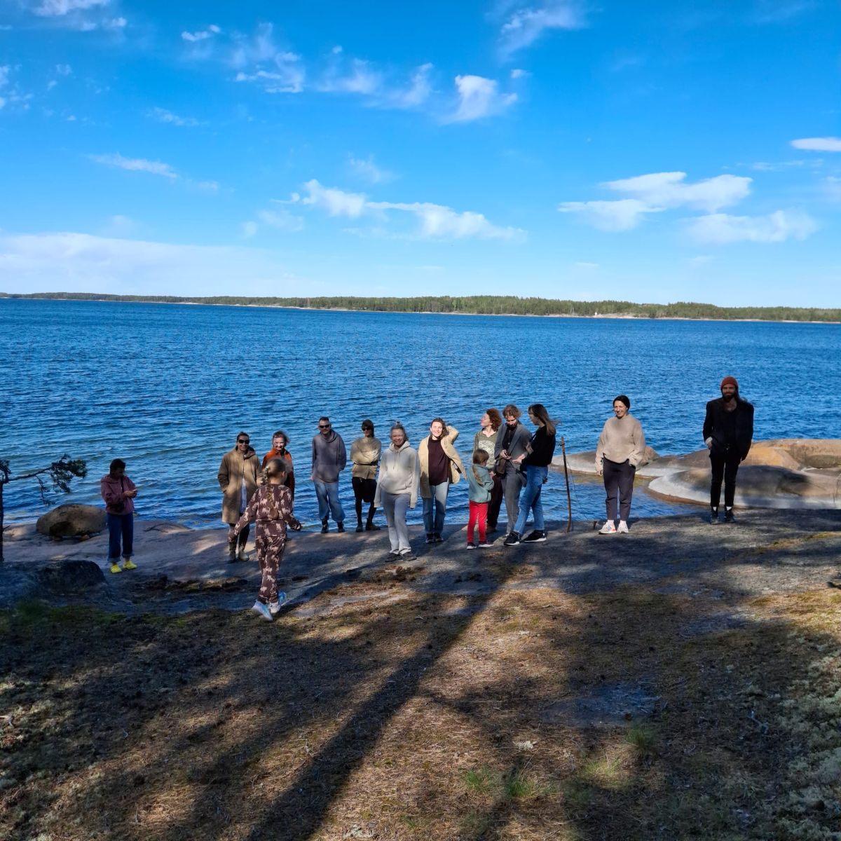 En grupp människor står på en klippig strand med havet i bakgrunden.